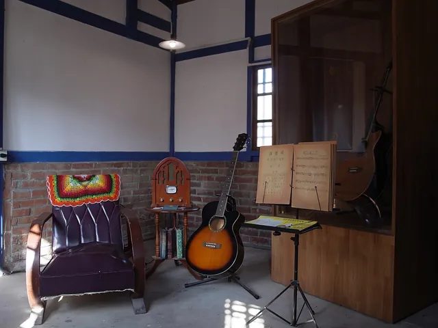吳晉淮音樂紀念館內一角(2021 年攝),用吉他、老收音機與譜架布置成的場景;畫面裡的吉他是不是他本人用過的琴,資料沒有說明。紀念館常態展示他的樂譜手稿、吉他與相關文物。