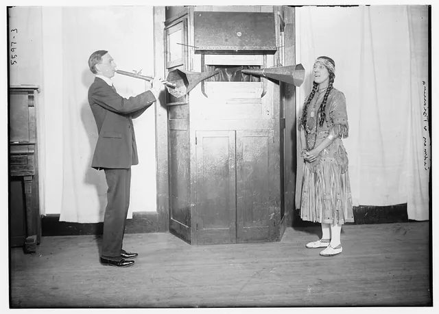 約 1920~1925 年,作曲家卡德曼(Charles Wakefield Cadman)吹長笛、歌手齊安妮娜(Tsianina Redfeather)唱歌,兩人各自對著從錄音機櫃伸出來的錄音喇叭筒演出,這就是電氣錄音以前的錄音方式